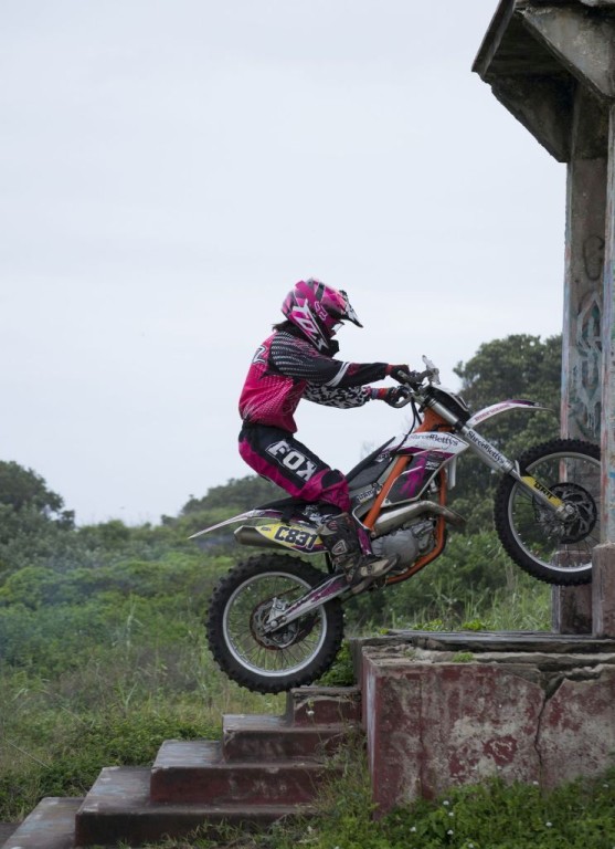 Woman dirt biker dressed in pink riding up some steps into a building
